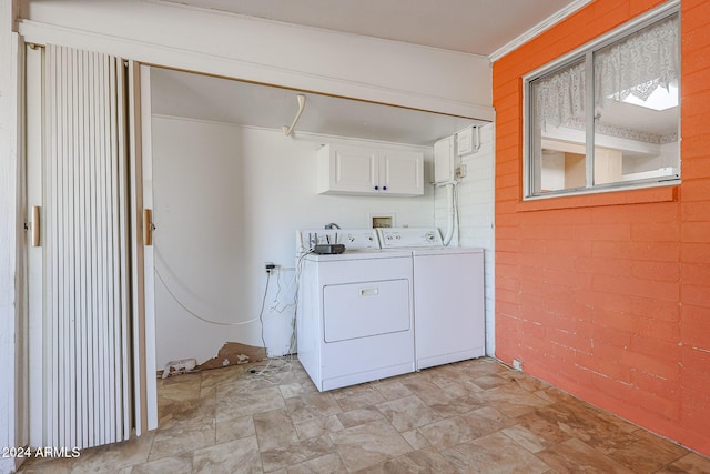 laundry area with cabinets, washer and clothes dryer, and brick wall