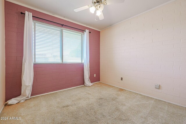 carpeted empty room with ceiling fan, crown molding, and brick wall