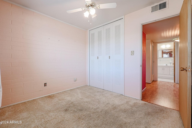 unfurnished bedroom featuring ceiling fan, a closet, brick wall, and light carpet