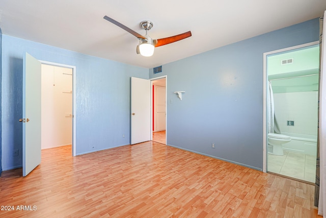 unfurnished bedroom with ensuite bathroom, a walk in closet, light hardwood / wood-style flooring, ceiling fan, and a closet