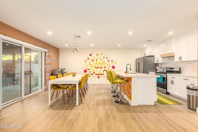 kitchen with sink, stainless steel appliances, an island with sink, pendant lighting, and white cabinets