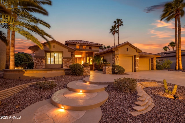 mediterranean / spanish house featuring an attached garage, stone siding, concrete driveway, and stucco siding