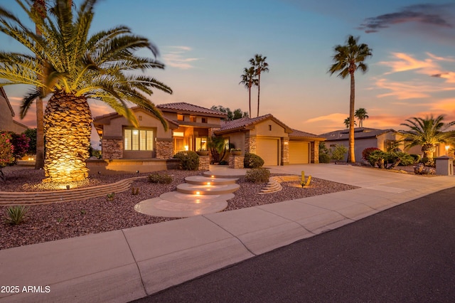 mediterranean / spanish-style home featuring an attached garage, a tile roof, stone siding, driveway, and stucco siding