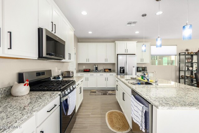 kitchen featuring white cabinetry, appliances with stainless steel finishes, hanging light fixtures, and a kitchen island with sink