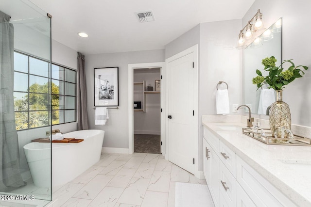 full bathroom with a healthy amount of sunlight, marble finish floor, a freestanding bath, and vanity