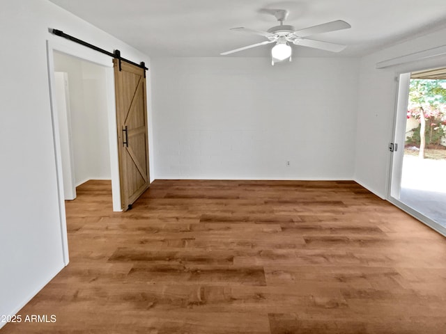 empty room featuring hardwood / wood-style flooring, a barn door, and ceiling fan