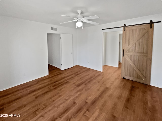 spare room featuring wood-type flooring, a barn door, and ceiling fan
