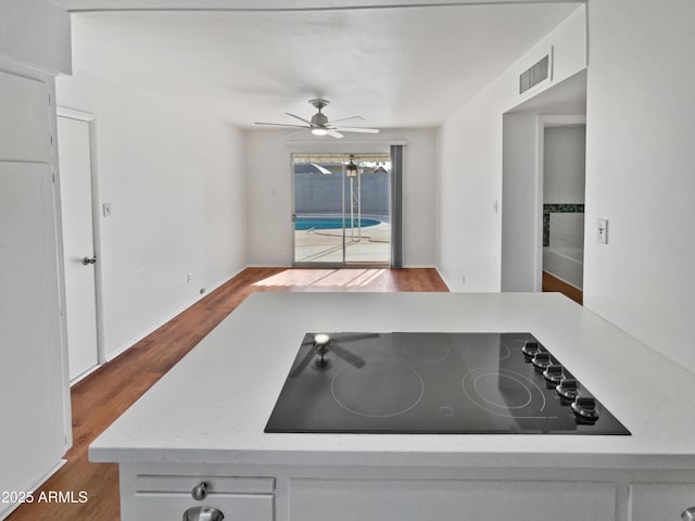 kitchen with black electric stovetop, white cabinets, ceiling fan, and light hardwood / wood-style flooring