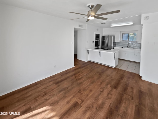 kitchen with tasteful backsplash, sink, white cabinets, a kitchen bar, and black appliances