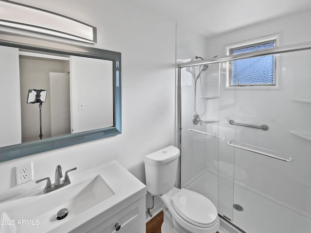 bathroom featuring a shower with door, vanity, and toilet