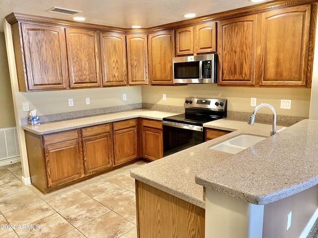 kitchen featuring appliances with stainless steel finishes, brown cabinets, a sink, and light stone counters