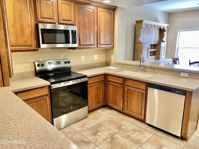 kitchen with appliances with stainless steel finishes, brown cabinetry, a sink, and light stone counters