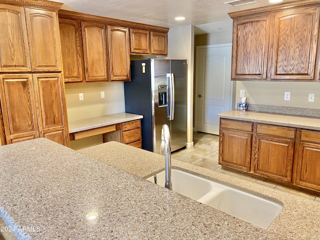 kitchen featuring brown cabinetry, built in study area, stainless steel fridge with ice dispenser, a textured ceiling, and a sink