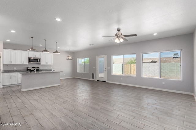 kitchen featuring stainless steel appliances, white cabinets, pendant lighting, light hardwood / wood-style flooring, and a center island with sink