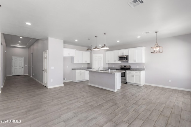 kitchen featuring a kitchen island with sink, stainless steel appliances, hanging light fixtures, white cabinetry, and light hardwood / wood-style flooring