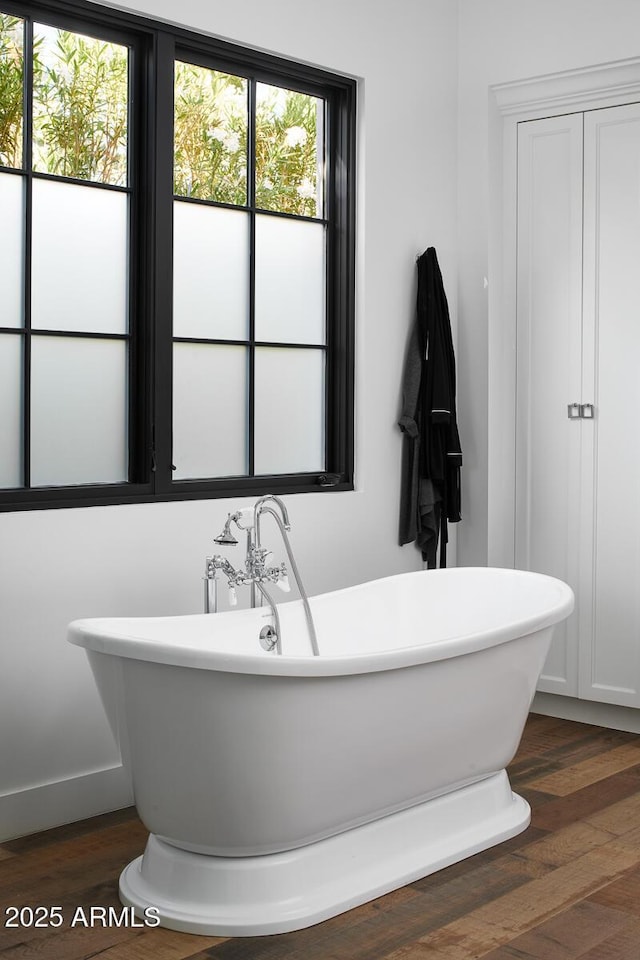 bathroom with a healthy amount of sunlight, a tub to relax in, and hardwood / wood-style flooring