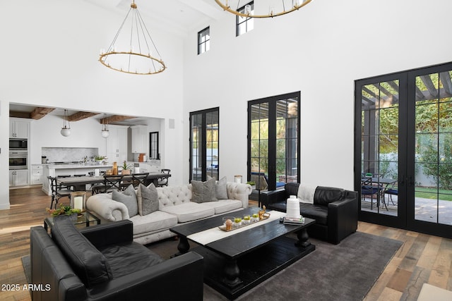 living room featuring french doors, an inviting chandelier, a towering ceiling, and dark hardwood / wood-style floors