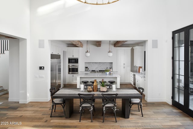 dining room with a towering ceiling, french doors, and light wood-type flooring