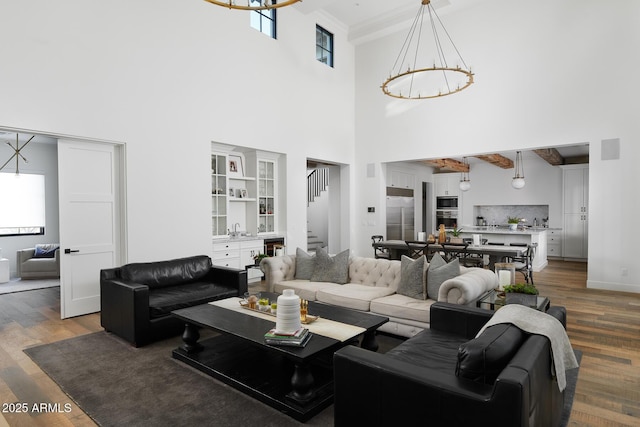 living room featuring an inviting chandelier, a towering ceiling, beamed ceiling, and wood-type flooring