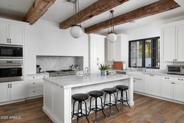 kitchen featuring a center island with sink, black microwave, oven, decorative light fixtures, and tasteful backsplash