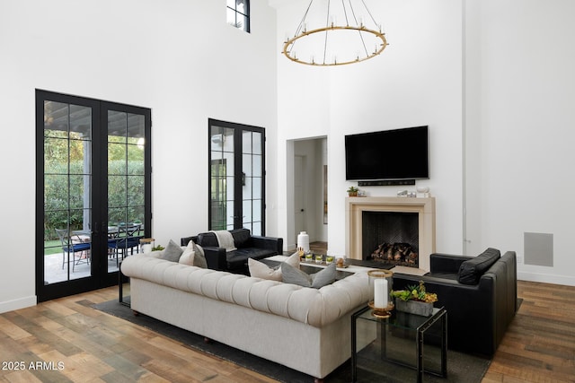 living room featuring french doors, a high ceiling, hardwood / wood-style floors, and a notable chandelier