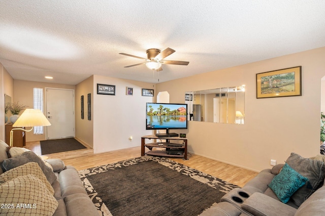 living area featuring a ceiling fan, a textured ceiling, baseboards, and wood finished floors