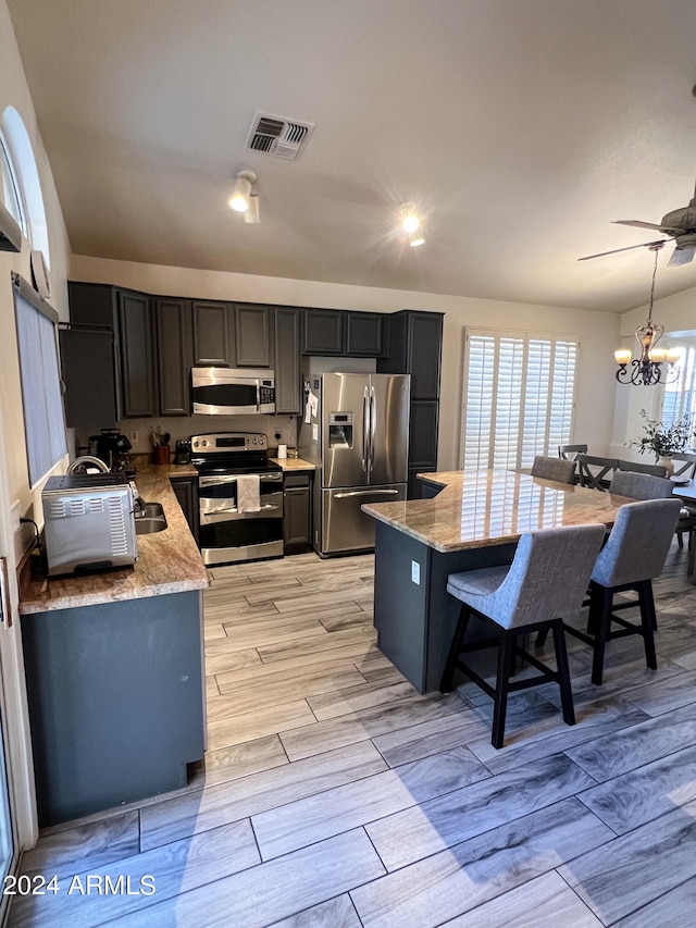 kitchen with stainless steel appliances, light stone counters, light hardwood / wood-style flooring, a breakfast bar area, and ceiling fan with notable chandelier