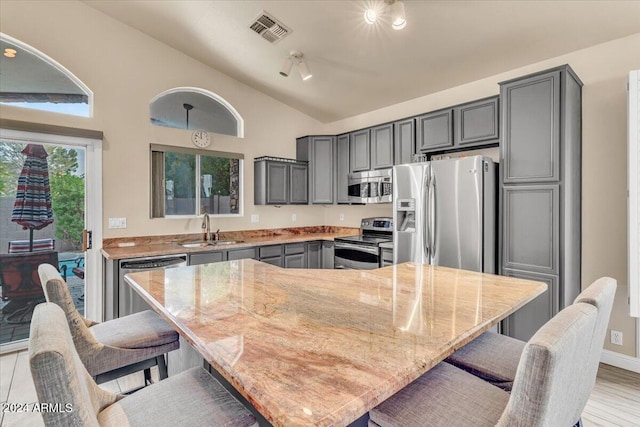 kitchen featuring appliances with stainless steel finishes, a kitchen island, sink, and light stone counters