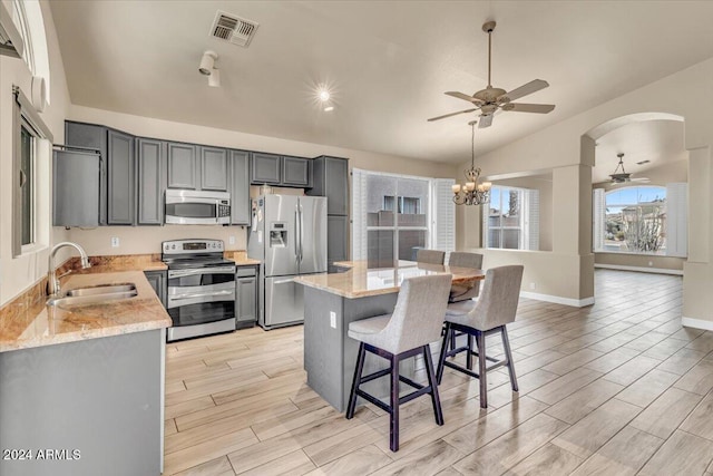 kitchen with gray cabinetry, stainless steel appliances, a center island, sink, and light stone counters