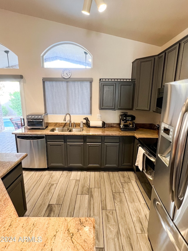 kitchen with appliances with stainless steel finishes, vaulted ceiling, plenty of natural light, and sink