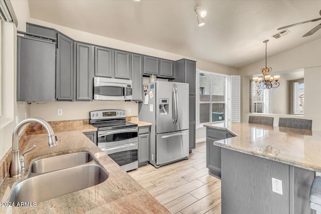 kitchen with appliances with stainless steel finishes, sink, pendant lighting, and light stone countertops