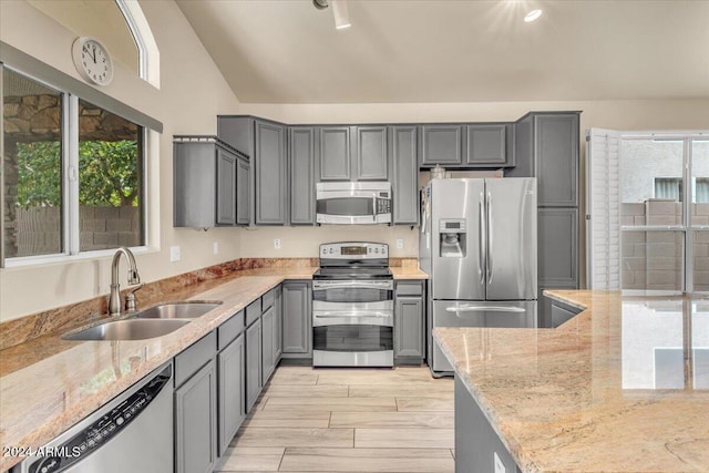 kitchen featuring sink, gray cabinets, vaulted ceiling, light stone counters, and appliances with stainless steel finishes