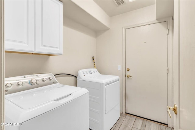 laundry room featuring cabinets, washing machine and clothes dryer, and light hardwood / wood-style floors