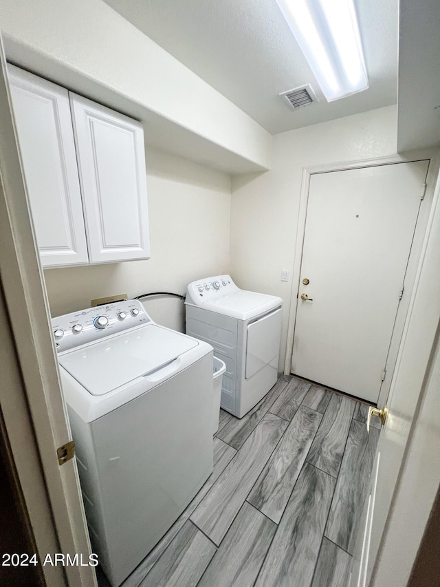 laundry area with washing machine and dryer, cabinets, and light wood-type flooring