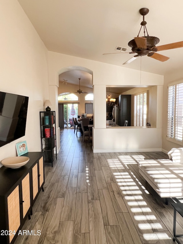 unfurnished living room with ceiling fan with notable chandelier, vaulted ceiling, and dark wood-type flooring