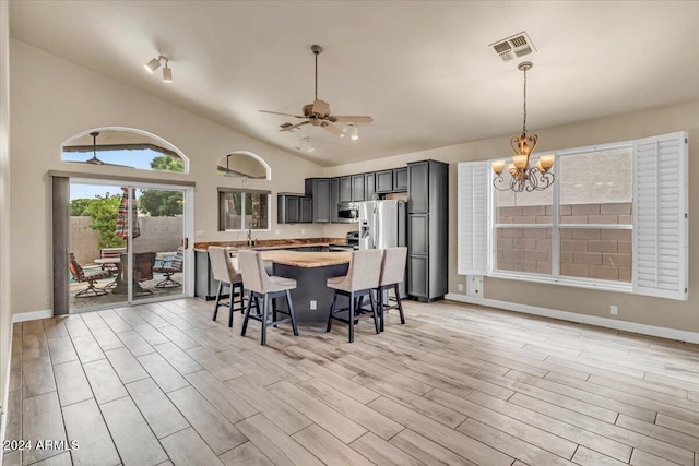 kitchen with light hardwood / wood-style flooring, hanging light fixtures, a breakfast bar area, stainless steel appliances, and ceiling fan with notable chandelier