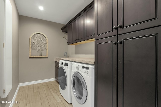 clothes washing area with cabinets, light hardwood / wood-style floors, and washing machine and dryer