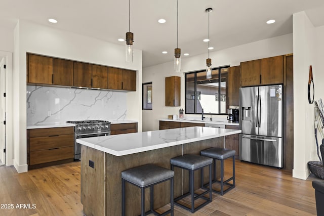 kitchen with stainless steel appliances, backsplash, wood finished floors, and pendant lighting