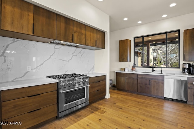 kitchen with light wood finished floors, backsplash, stainless steel appliances, a sink, and recessed lighting