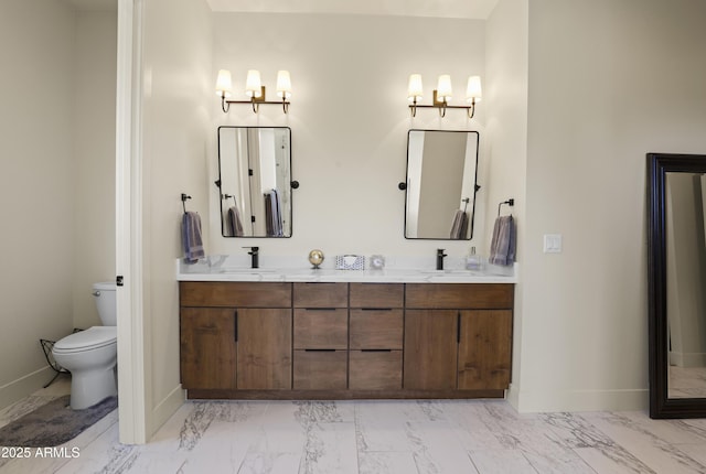 full bath with toilet, double vanity, baseboards, and a sink