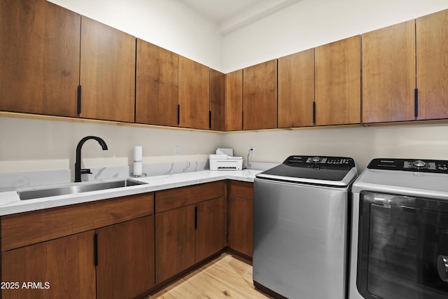 laundry room with washing machine and dryer, light wood-type flooring, a sink, and cabinet space