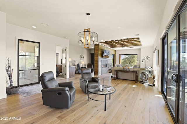 living area with light wood-type flooring, a large fireplace, visible vents, and a notable chandelier