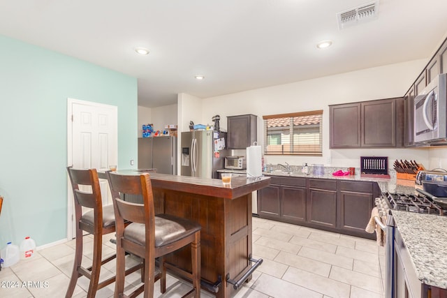 kitchen with stainless steel appliances, dark brown cabinetry, visible vents, and a center island