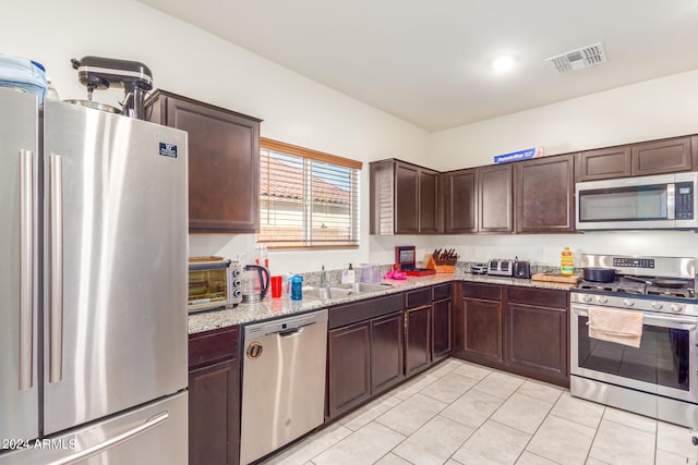 kitchen with light stone counters, stainless steel appliances, a sink, visible vents, and dark brown cabinets