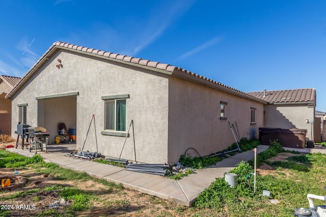 rear view of property with a tile roof, a patio, a hot tub, and stucco siding