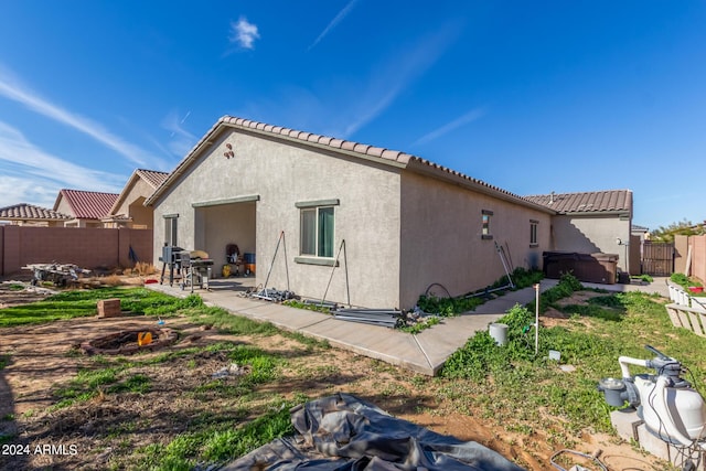 back of property featuring a fenced backyard, a tile roof, stucco siding, a patio area, and a hot tub