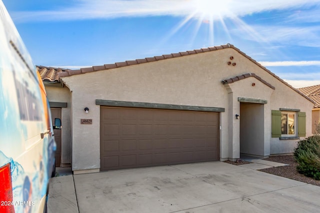 mediterranean / spanish house with a garage, driveway, a tile roof, and stucco siding