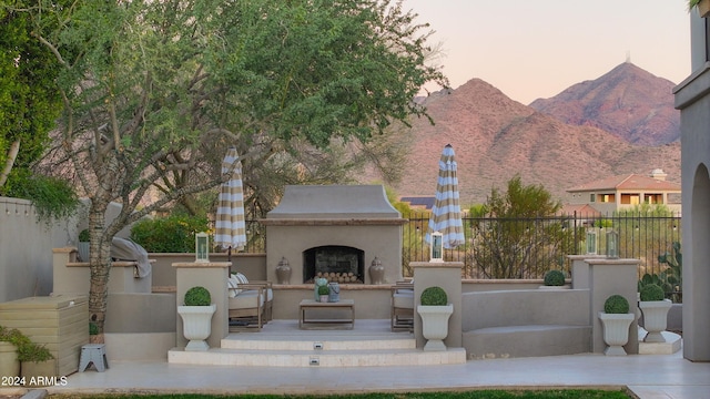 patio terrace at dusk featuring a mountain view and exterior fireplace