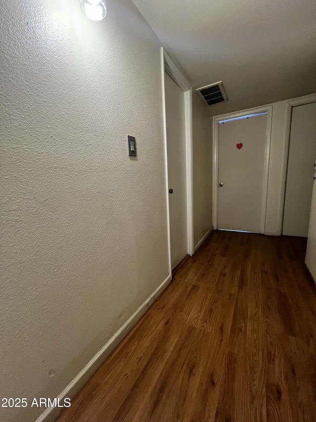 hallway featuring wood finished floors, baseboards, and a textured wall