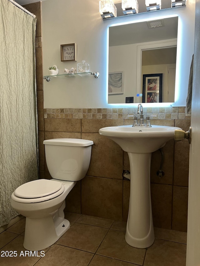 bathroom featuring tile patterned floors, tile walls, toilet, a wainscoted wall, and a shower with curtain